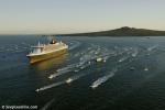 ID 3738 QUEEN MARY 2 (2003/148528grt/IMO 9241061) escorted by a flotilla of welcoming pleasurecraft and commercial tugs and ferries, with Rangitoto Island in the background, enters Aucklands' Waitemata...
